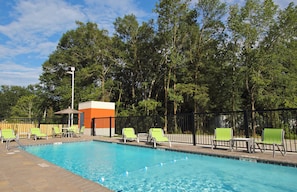 Una piscina con sillones de descanso y un pequeño pabellón, rodeado de árboles.