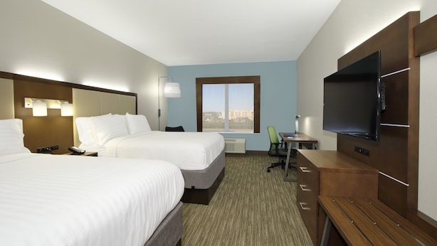 A hotel room with two beds, a desk, a chair, a TV, and a window with a city view.