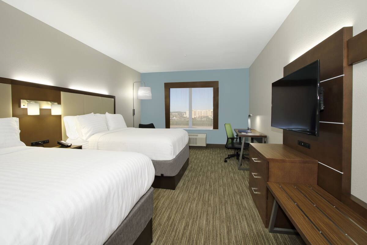 A hotel room with two beds, a desk, a chair, a TV, and a window with a city view.