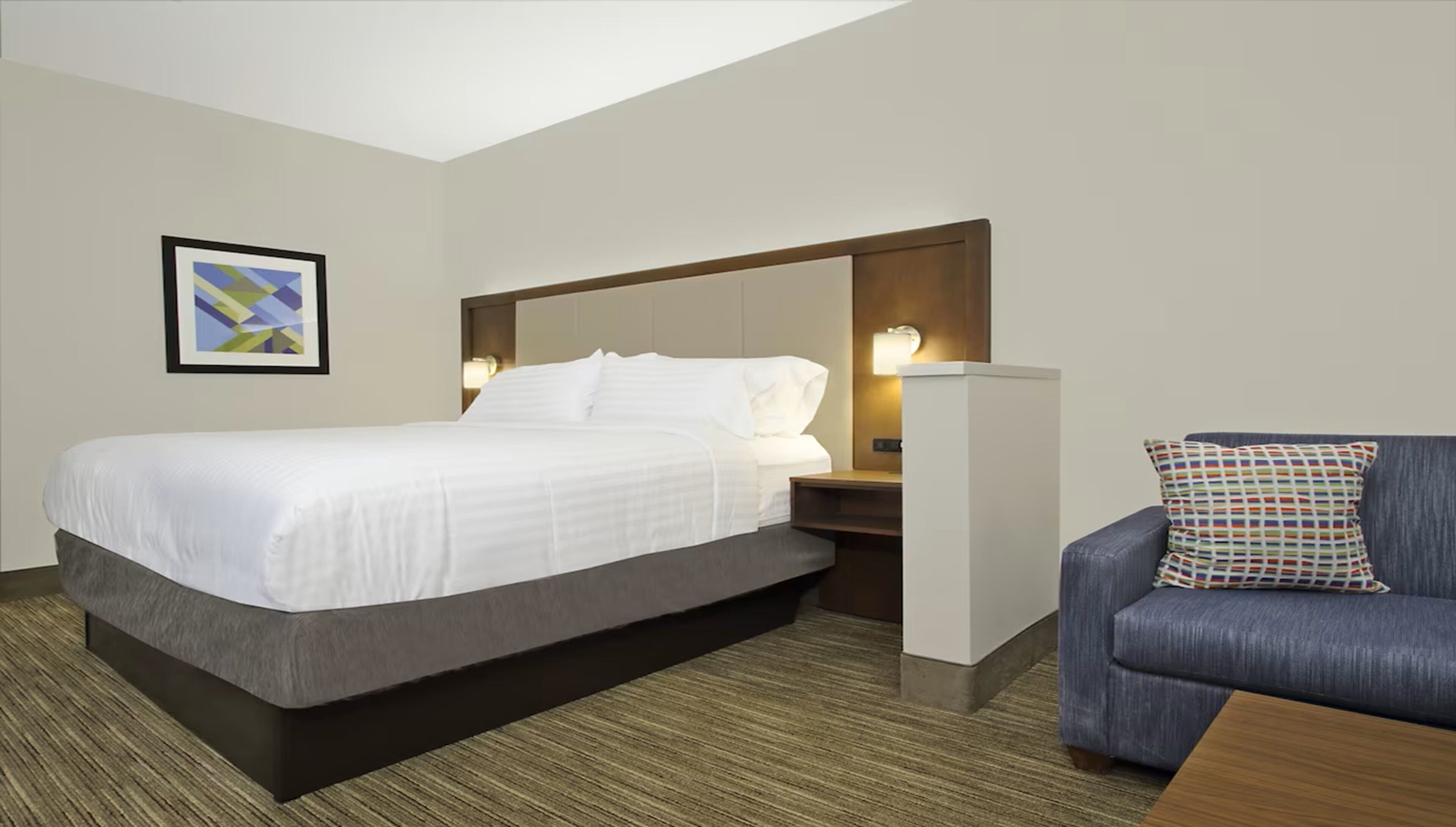 Una habitación de hotel con cama, mesita de noche, lámpara y un sillón azul.