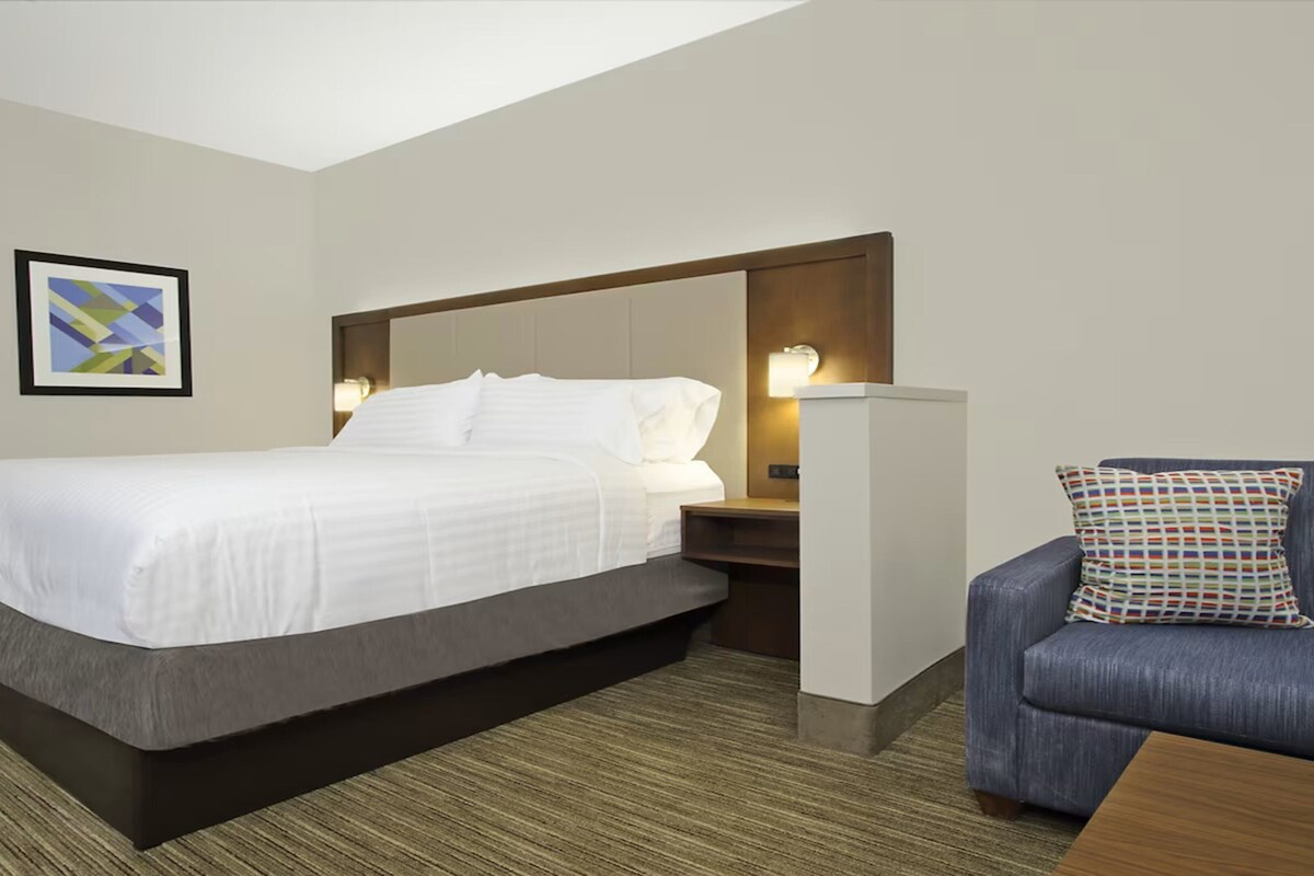 Een hotelkamer met een bed, een nachtkastje, een stoel en een lijst met een foto aan de muur.