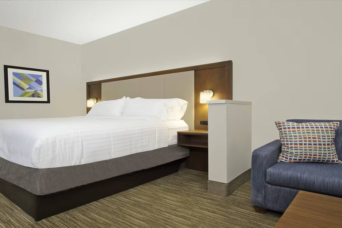 A hotel room with a bed, a nightstand, a chair, and a framed picture on the wall.