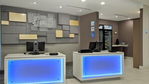A reception area with two reception desks, a wall-mounted sign, a refrigerator, and a patterned floor.