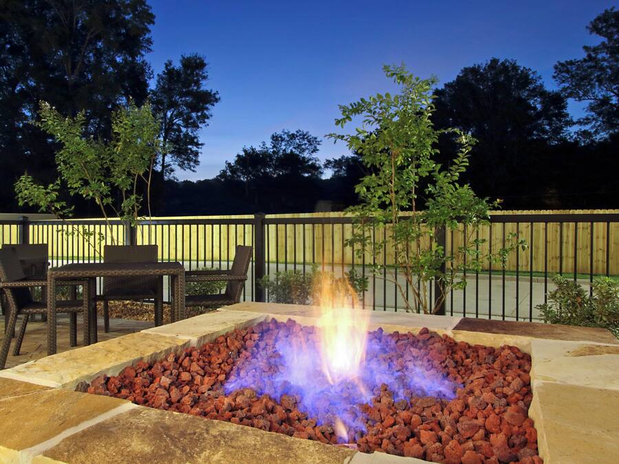 An outdoor fire pit surrounded by stone seating and a wooden fence.