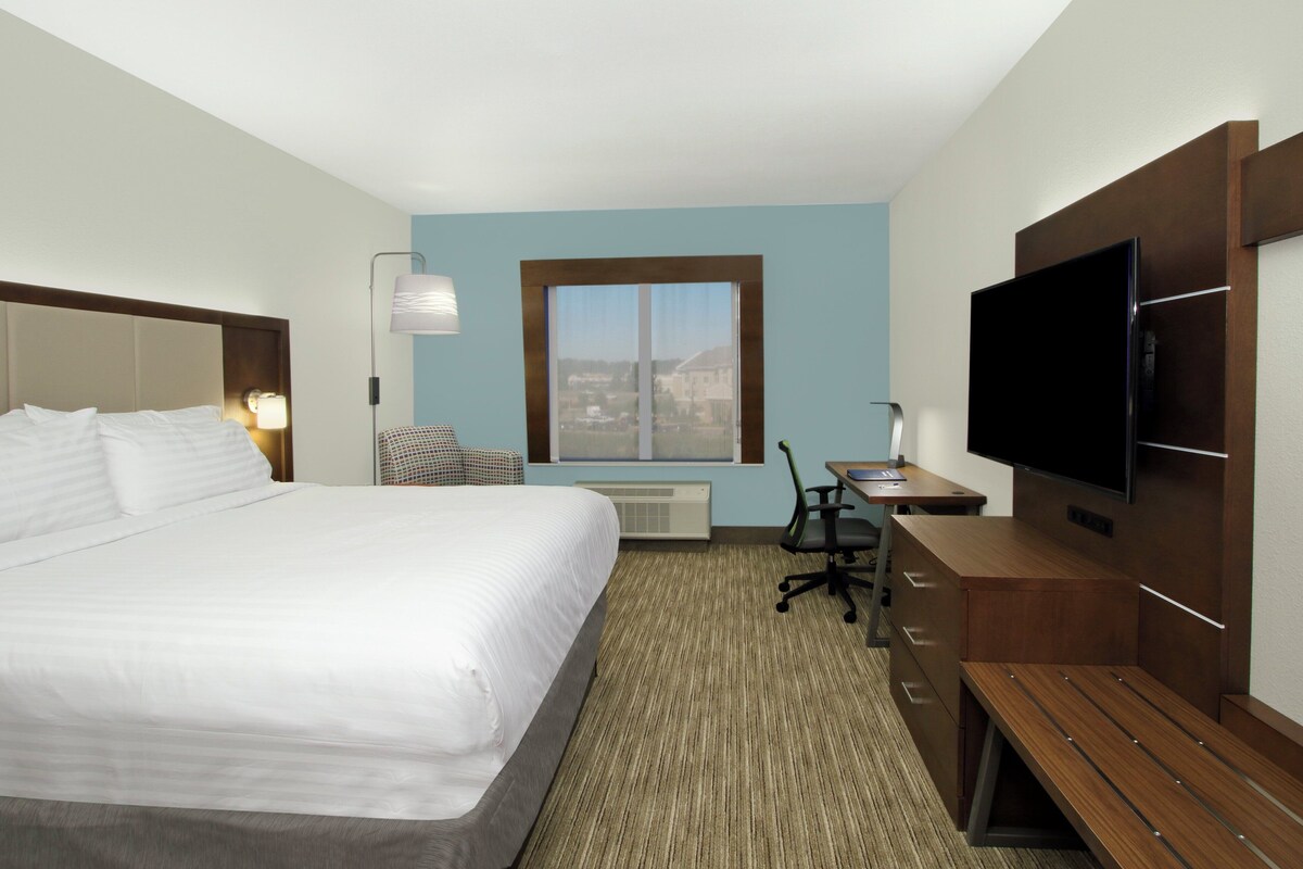 Een hotelkamer met een groot bed, een bureau met stoel, een televisie en een raam met uitzicht.