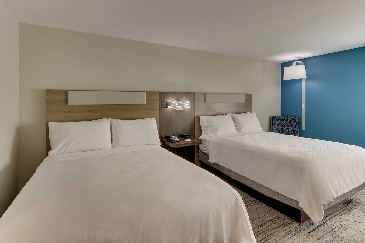 Een hotelkamer met twee bedden, een nachtkastje met een telefoon en een wandlamp.