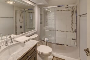A modern bathroom with a glass-enclosed shower, a marble sink, and a toilet.