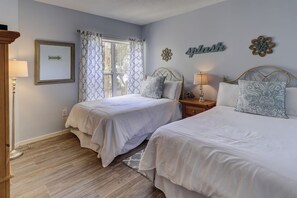 A bedroom with two beds, a window with patterned curtains, a wall clock, and a directional sign.