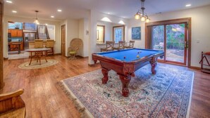 A spacious room with a pool table, wooden flooring, and a large rug.
