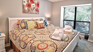 Un dormitorio con cama, ventilador de techo, ventana con persianas y un cuadro en la pared.
