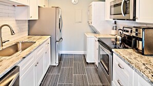 Una cocina moderna con armarios blancos, un refrigerador de acero inoxidable, un microondas y una estufa.