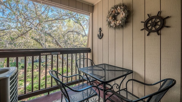 A balcony with a metal table and chairs, a wreath, and a ship's wheel decoration.