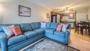 A living room with a sectional sofa, a dining area, and a kitchen in the background.