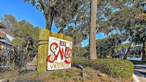 A sign for SANS Village with a rustic wooden fence and greenery around it.