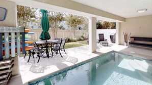 Ein überdachter Bereich mit einem Pool, einem Tisch, Stühlen, einer Bank und einem Zaun im Hintergrund.
