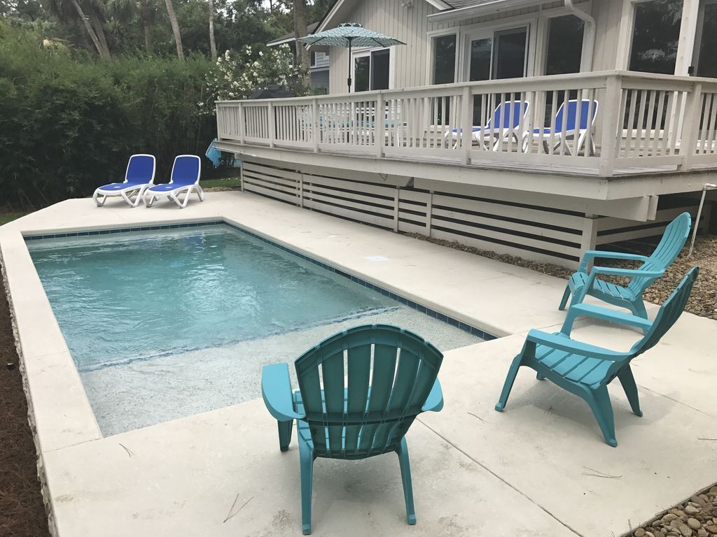 A swimming pool with a deck, two blue chairs, and a covered area with umbrellas.