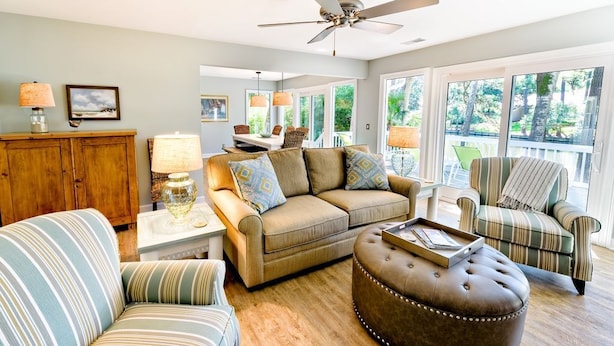 A spacious living room with a sofa, ottoman, and armchair, a wooden cabinet, and a ceiling fan. - Palmetto Paradise 3 Bedroom Holiday Home (Hilton Head Island)