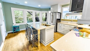 A modern kitchen with a central island, white cabinetry, and a large window providing a view of greenery. - Palmetto Paradise 3 Bedroom Holiday Home (Hilton Head Island)