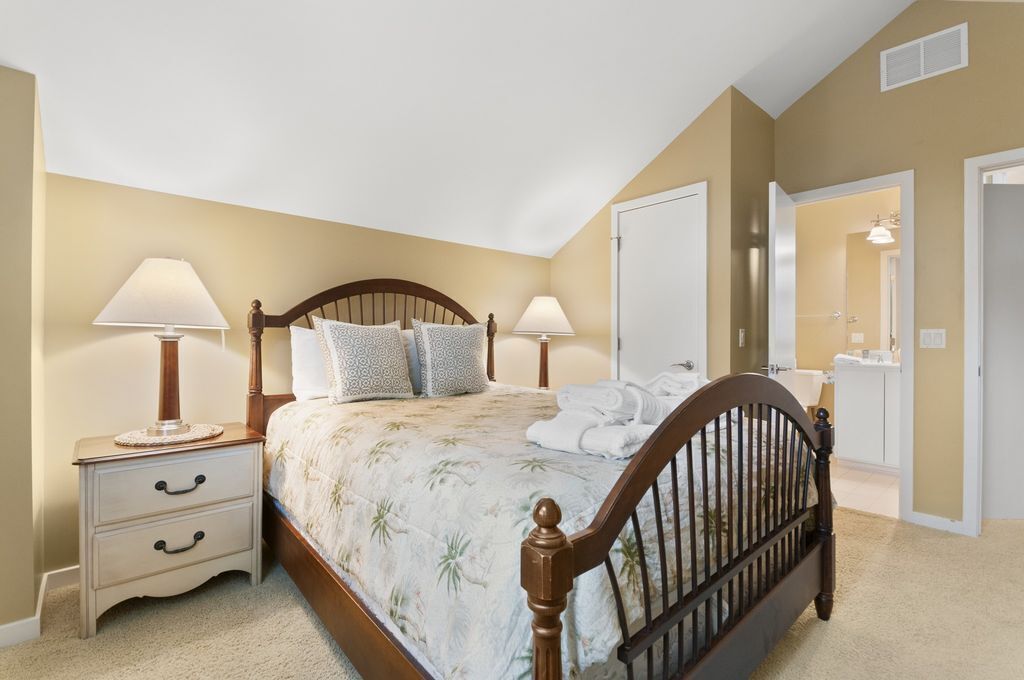 A bedroom with a bed, two bedside tables, a nightstand, a mirror, and a door leading to a bathroom.
