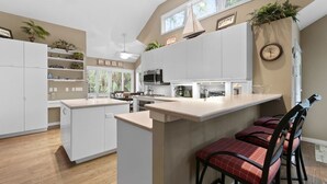 Une cuisine moderne avec des meubles blancs, un îlot central et un coin repas doté de chaises rouges.