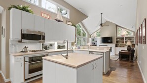 Une cuisine moderne avec des meubles blancs, un îlot central, des appareils en acier inoxydable et un ventilateur de plafond.