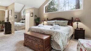 Une chambre avec une grande fenêtre, un lit recouvert de draps blancs, une commode en bois et une table de chevet avec des lampes.