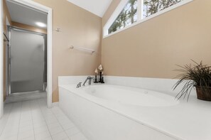 Een moderne badkamer met een ruime badkuip, douche en een raam voor natuurlijk licht.