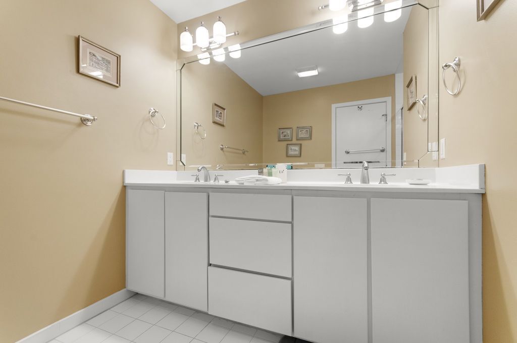A modern bathroom with a large mirror, white cabinets, and a towel rack.
