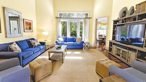 A living room with a blue sofa, a striped armchair, a wooden coffee table, and a television on a wooden cabinet. - Su Casa 5 Bedroom Holiday Home (Hilton Head Island)