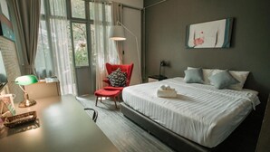 A modern hotel room with a large bed, a desk, a chair, and a window with curtains. - J Poshtel Chiangmai (Chiang Mai)