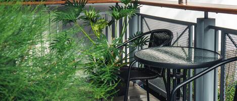A balcony with a metal table and chairs, surrounded by potted plants and a metal railing.