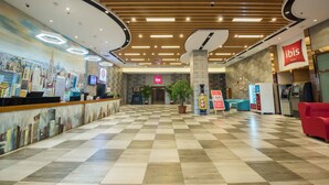 A hotel lobby with a checkered floor, a reception desk, a large potted plant, a vending machine, and a red seating area. - ibis Daqing Haofang (Daqing)