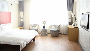 A hotel room with a bed, two wicker chairs, a small table with a vase of flowers, a bedside table with a lamp, and a TV on the wall. - ibis Daqing Haofang (Daqing)