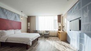 A hotel room with a bed, two chairs, a small table, a TV, and a large window with curtains. - ibis Daqing Haofang (Daqing)