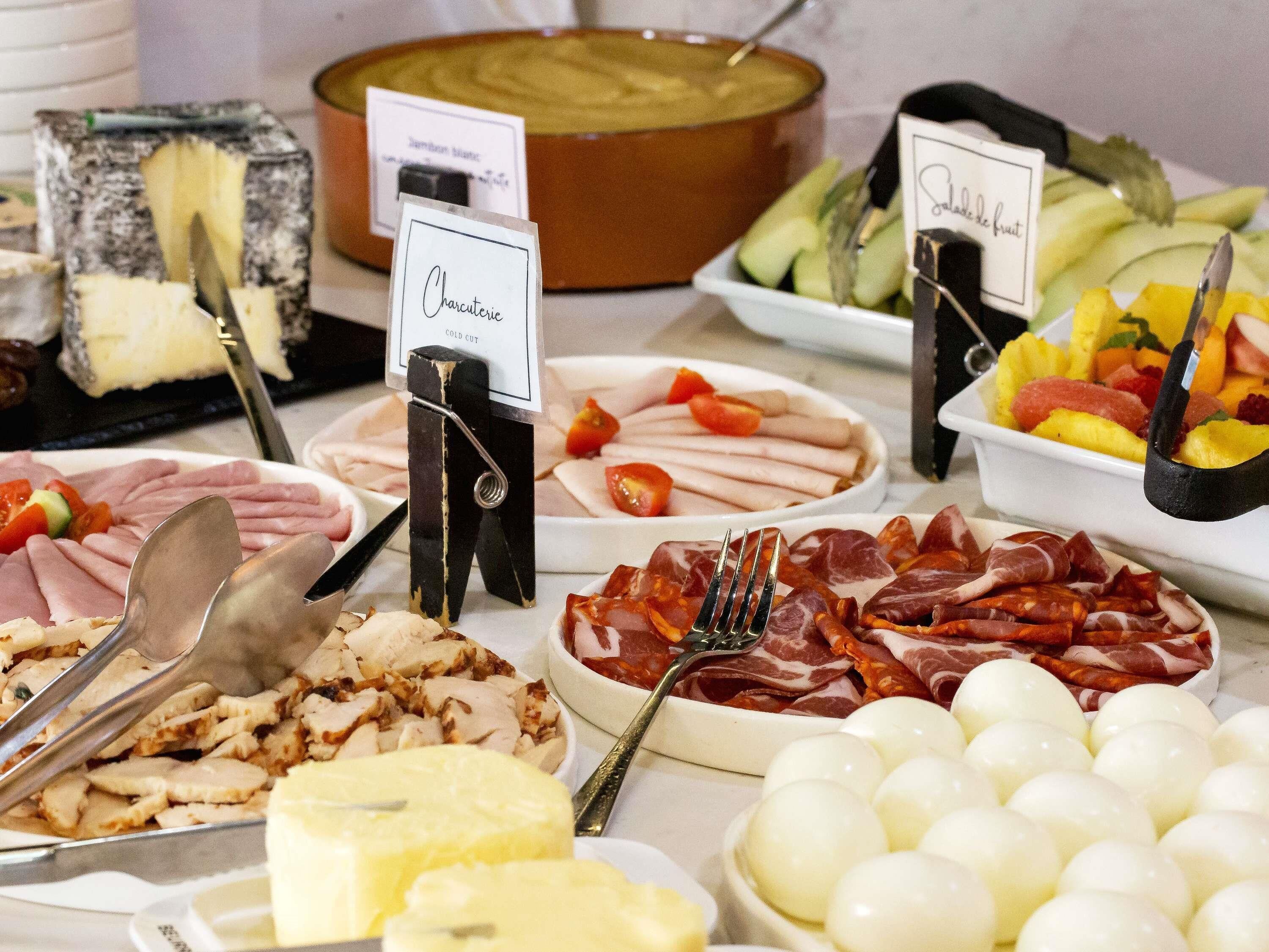 A buffet with various cold cuts, cheeses, and fruits.