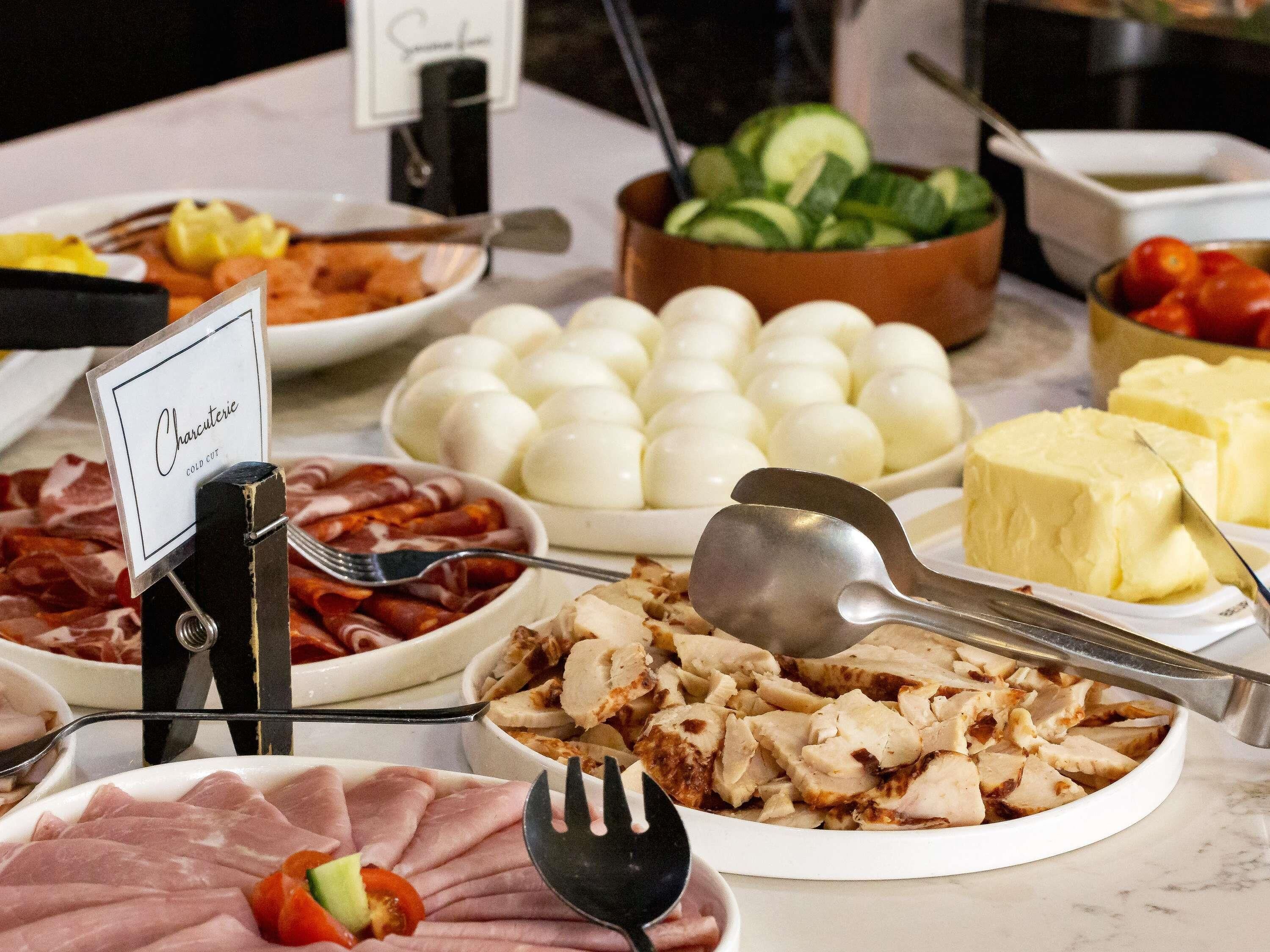 A buffet with various food items including cold cuts, boiled eggs, and cheese.
