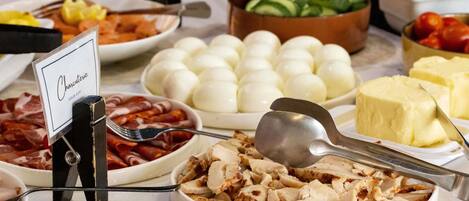 A buffet with various food items including cold cuts, boiled eggs, and cheese.