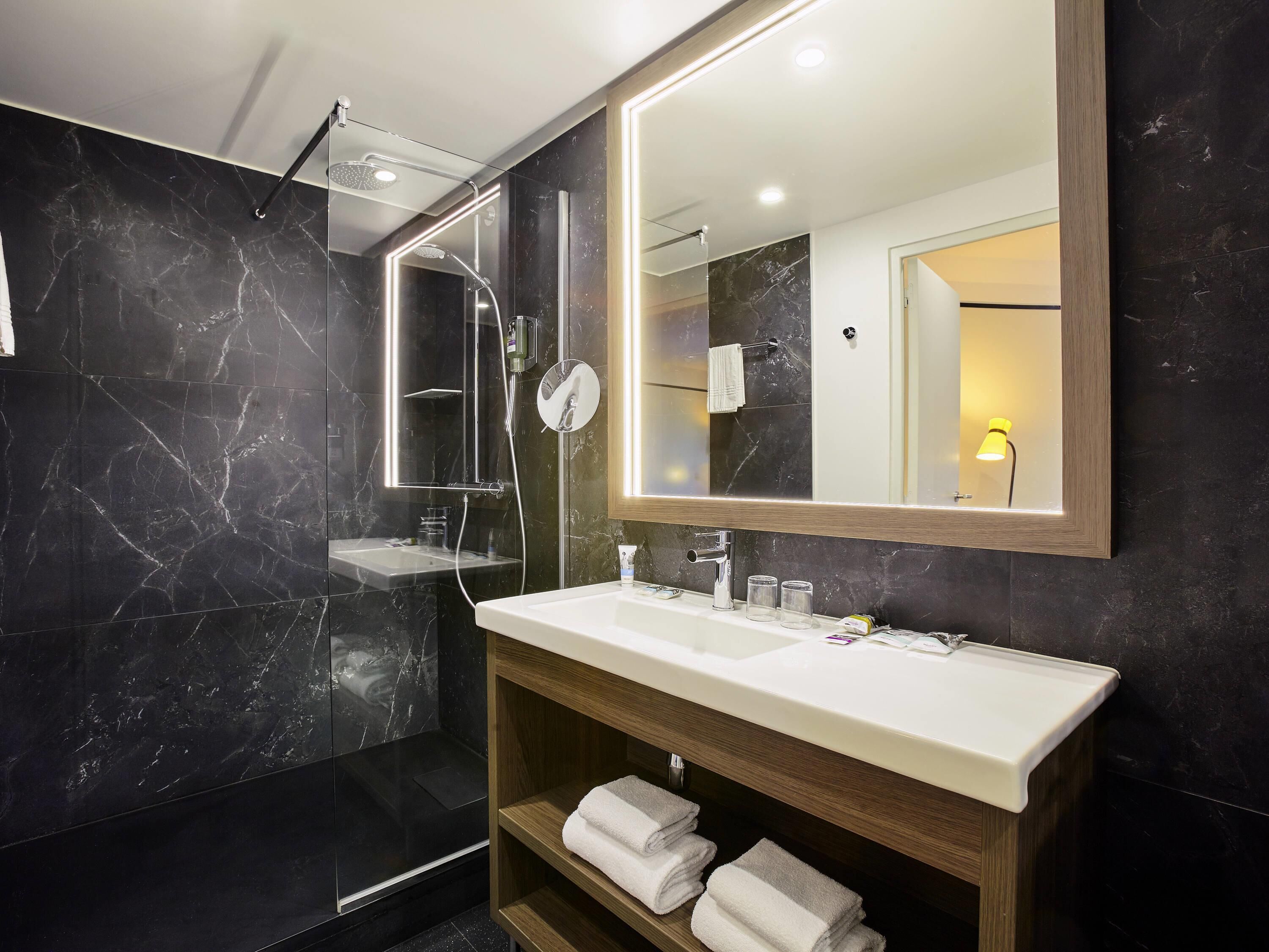 A modern bathroom with a glass-enclosed shower, a large mirror, and a wooden vanity with a sink.