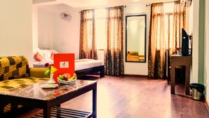 Um quarto com uma cama, um sofá, uma mesa com um vaso de flores e uma TV em um suporte.