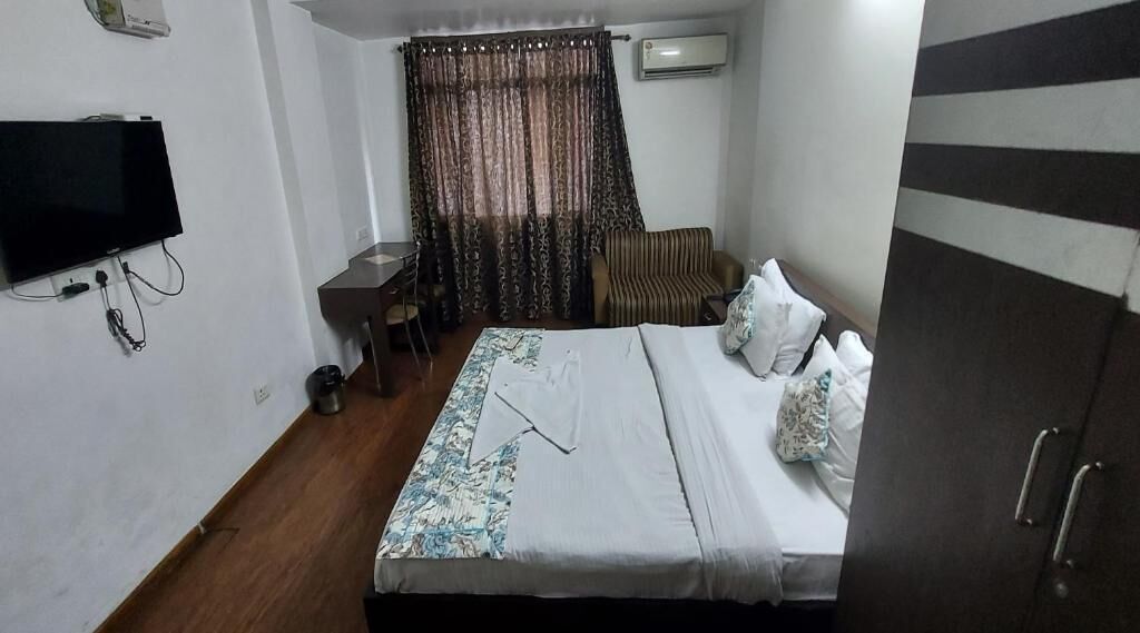 A hotel room with a bed, a desk, a chair, a television, and an air conditioning unit.