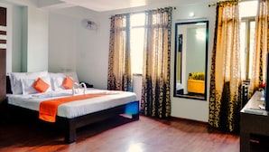 Quarto de hotel com cama, cortinas, espelho e escrivaninha.
