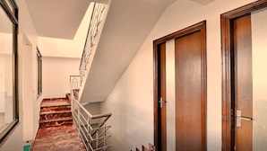 Um corredor com escadaria de mármore, portas de madeira e uma porta de vidro.