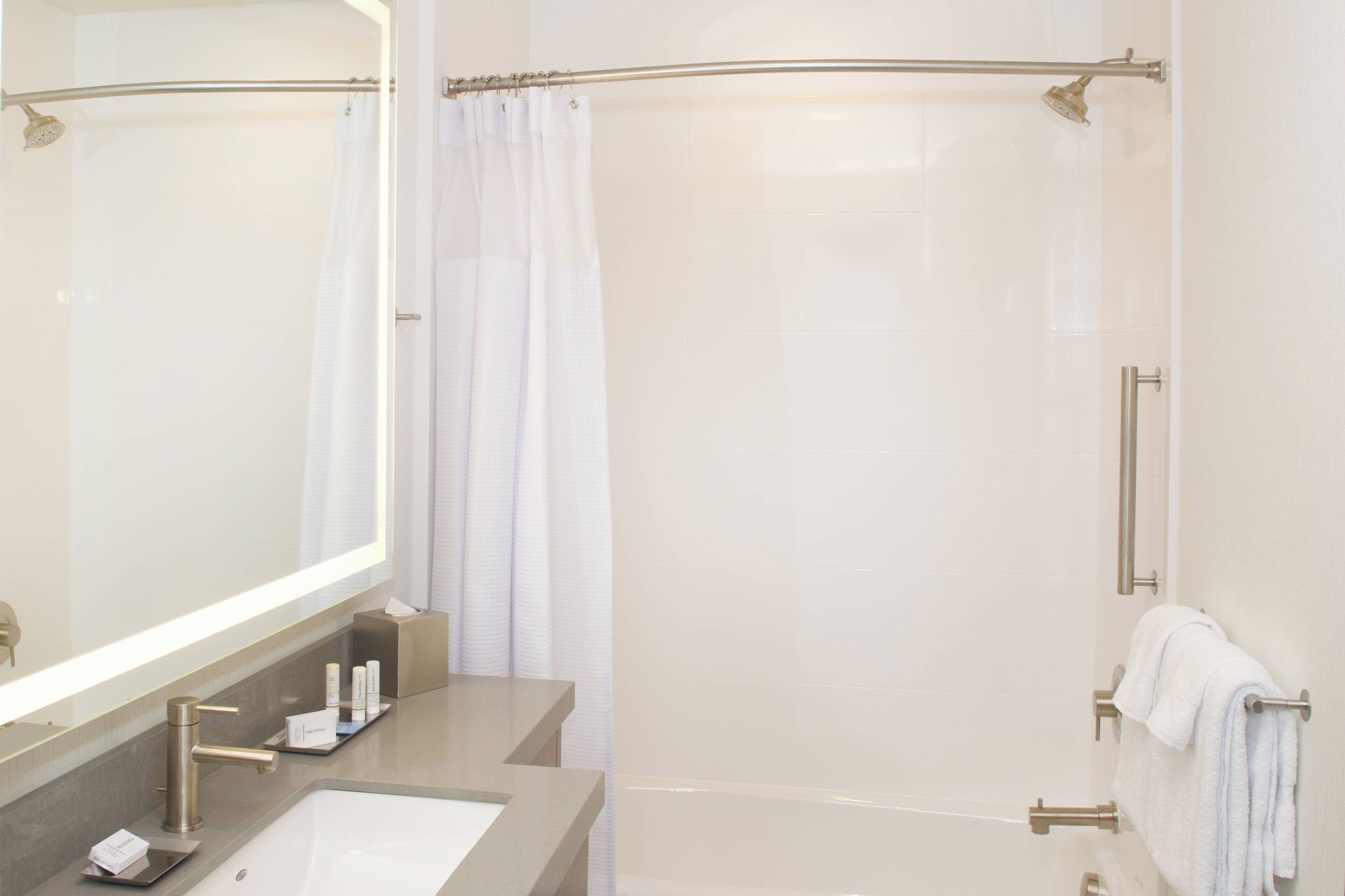 A modern bathroom with a large mirror, a sink, a shower, and a towel rack.