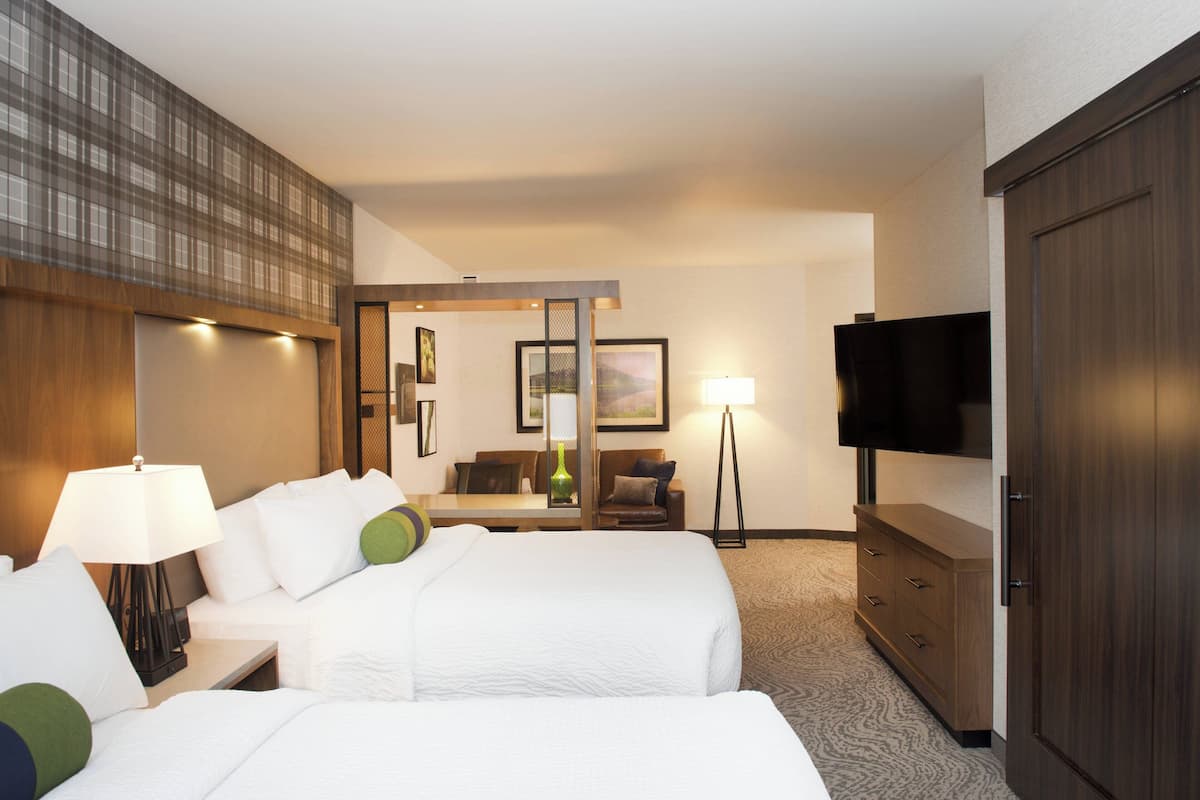 Habitación de hotel con dos camas, televisor, escritorio con lámpara, cómoda y espejo.