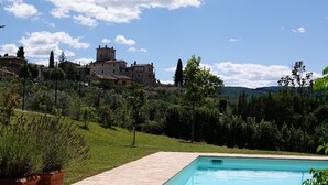 Une piscine dotée d’une terrasse carrelée, entourée de verdure et offrant une vue sur un bâtiment historique en arrière-plan.