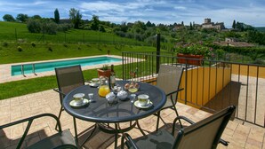 Une terrasse avec piscine, des sièges extérieurs et une vue sur un village.