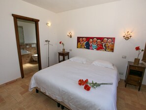 Une chambre à coucher avec un lit, un tableau au mur, un miroir, une table de chevet et un vase avec des fleurs.