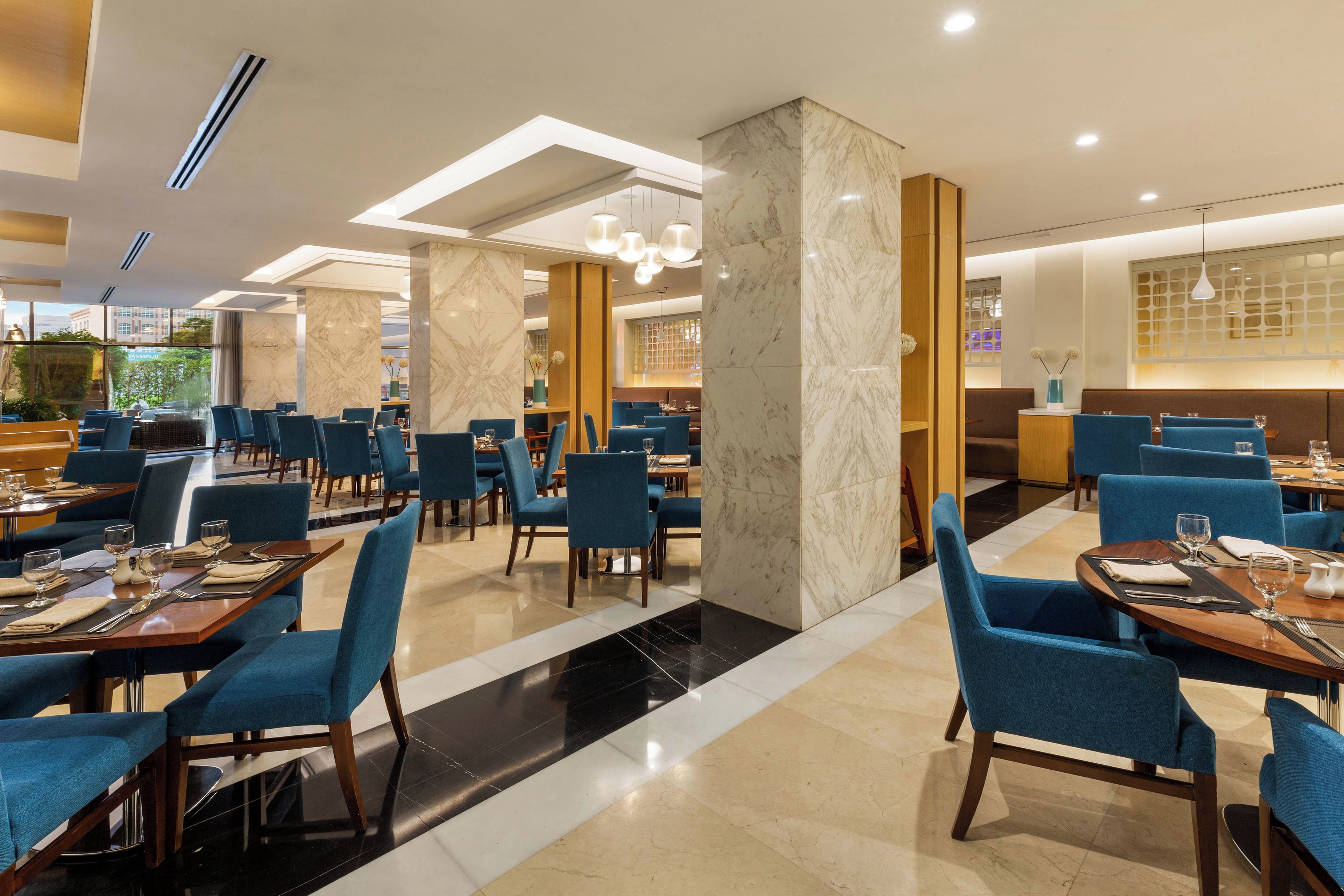 A modern restaurant interior with marble columns, blue upholstered chairs, and a clean, well-lit ambiance.