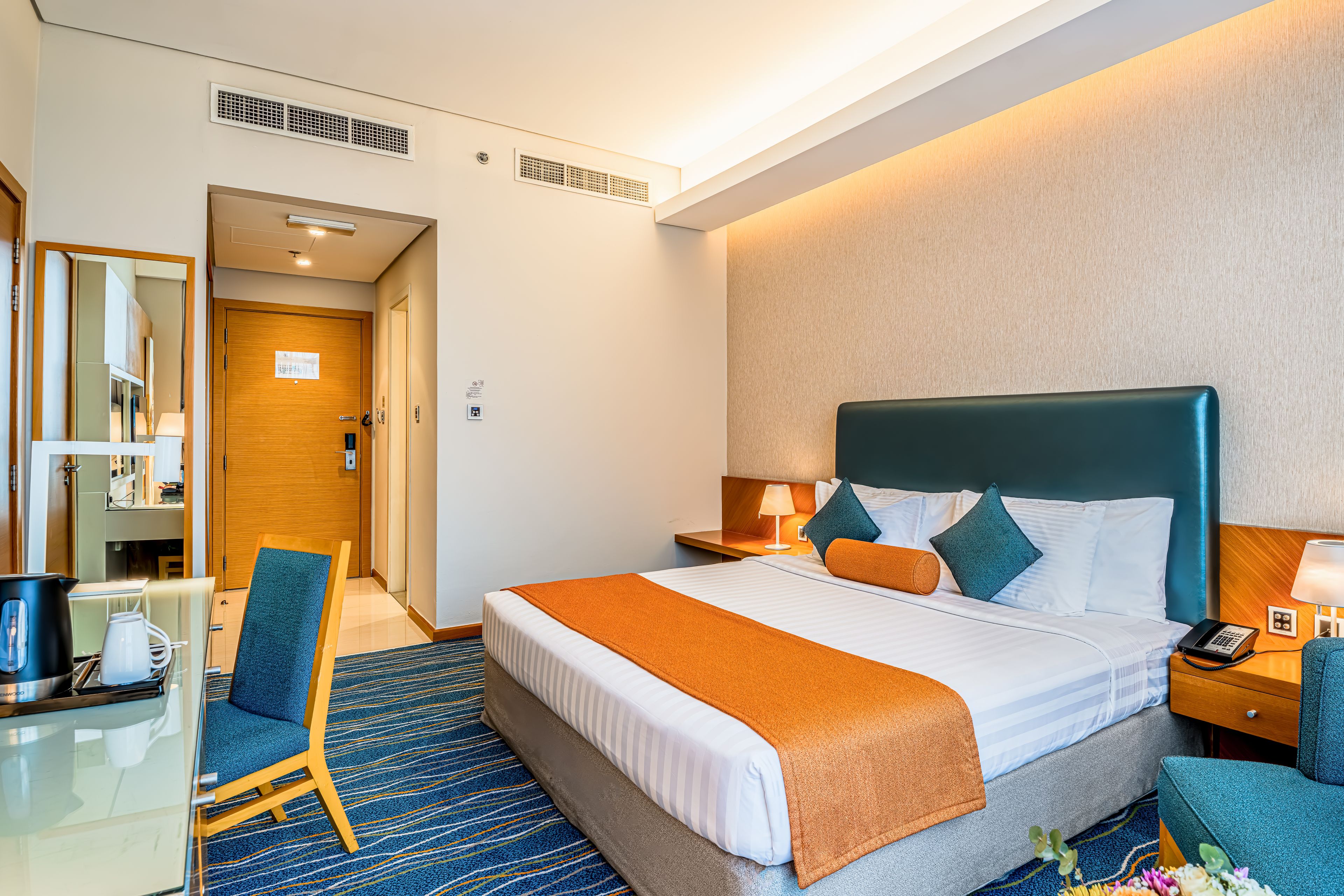Une chambre d’hôtel équipée d’un lit, d’une table de chevet, d’une lampe, d’une chaise et d’un bureau avec une bouilloire et une machine à café.