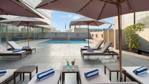 A rooftop pool area with lounge chairs, umbrellas, and a swimming pool. - Royal Continental Hotel (Dubai)